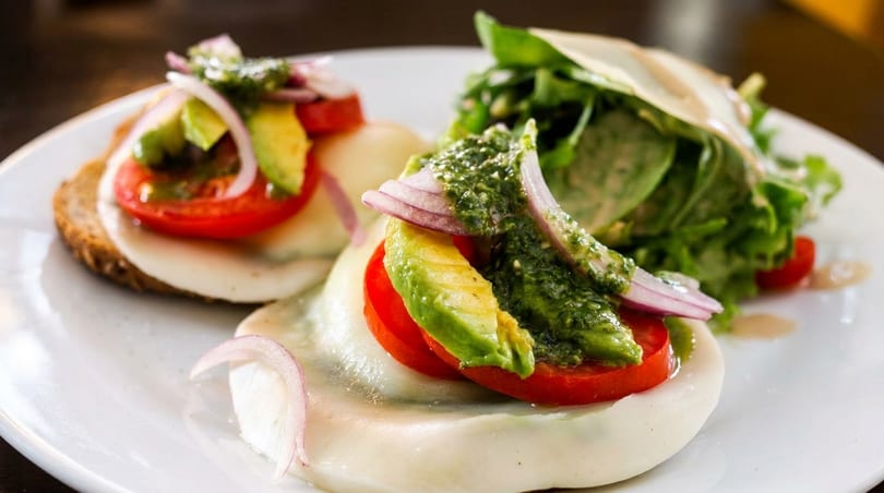 Two caprese-style appetizers with mozzarella, tomato, avocado, red onion, pesto, and a side salad.