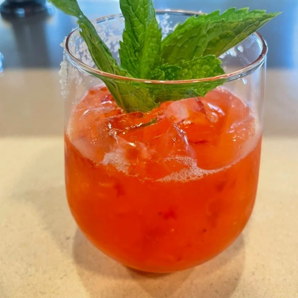 Bright red iced cocktail garnished with fresh mint leaves, served in a clear glass on a restaurant table.
