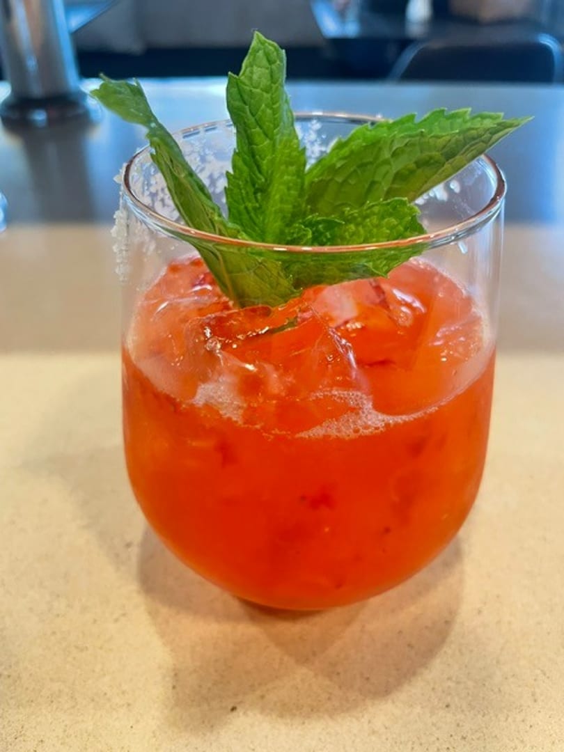 Red cocktail with ice, fresh mint garnish, and a sugared rim in a clear glass.