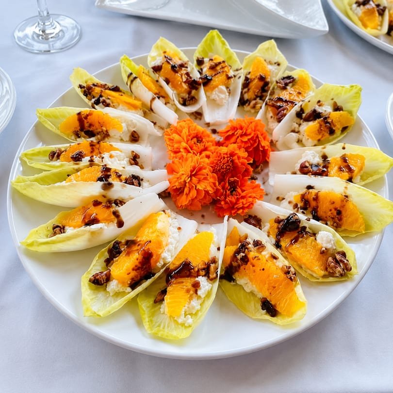 Endive leaves filled with orange, white cheese, nuts, and balsamic glaze, garnished with orange flowers.