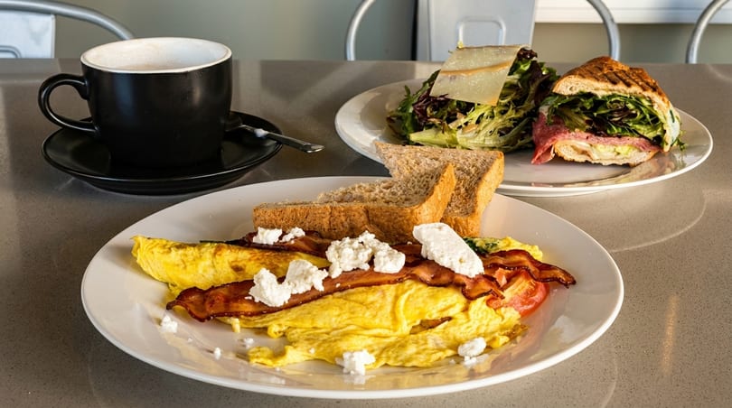 Breakfast omelet with bacon, feta, and toast, alongside a panini, salad, and coffee.