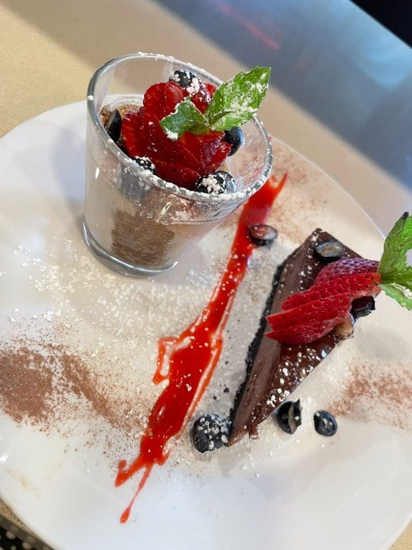 Decadent chocolate mousse and cake slice with fresh berries, mint, and strawberry sauce.