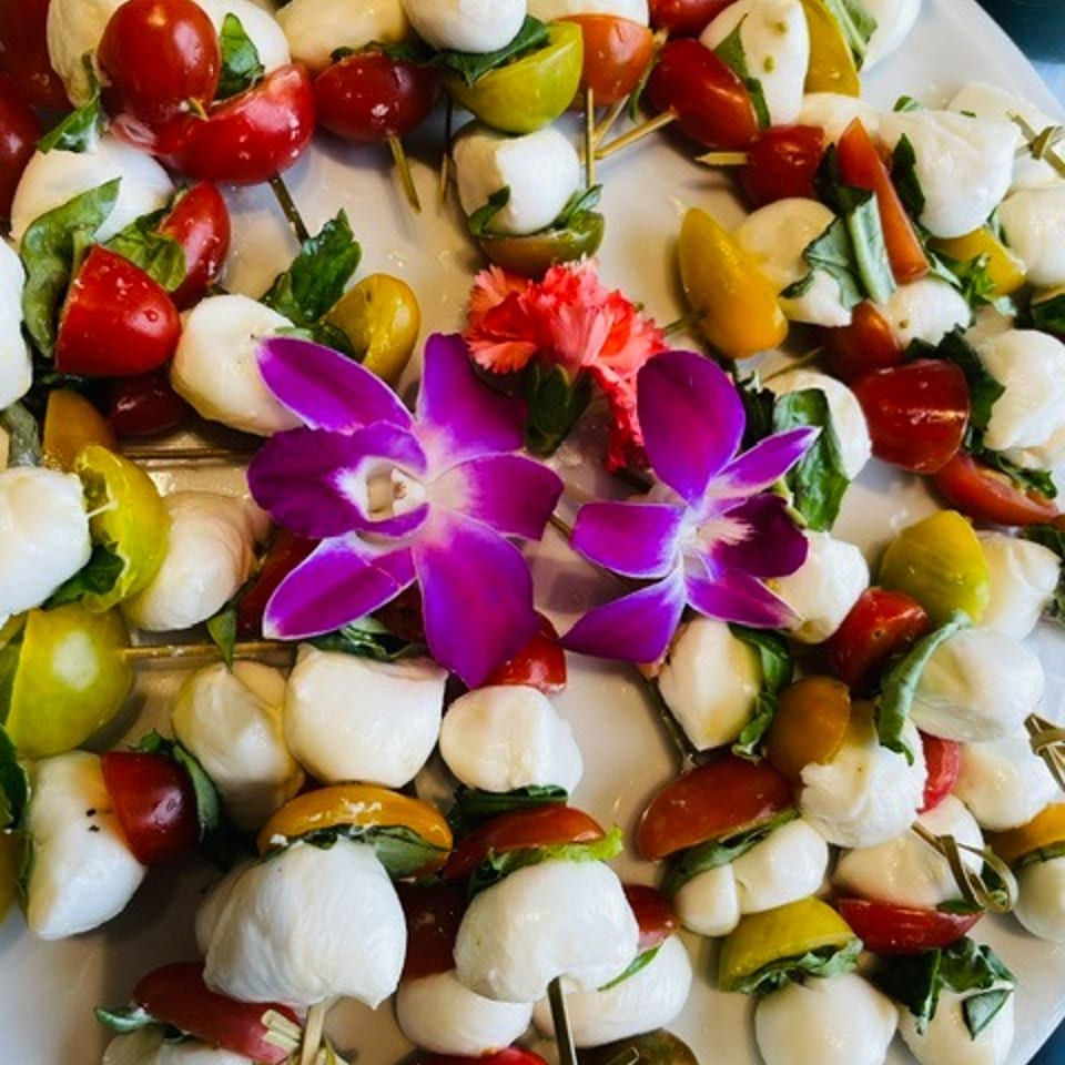 Colorful caprese skewers with mozzarella, cherry tomatoes, basil, and edible purple flowers arranged on a platter.