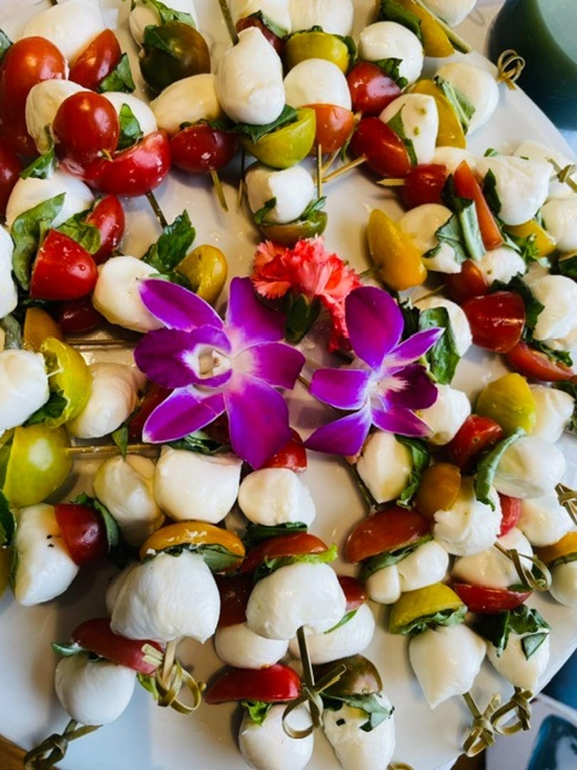 Numerous Caprese skewers with mozzarella, colorful cherry tomatoes, and basil, garnished with purple orchids.