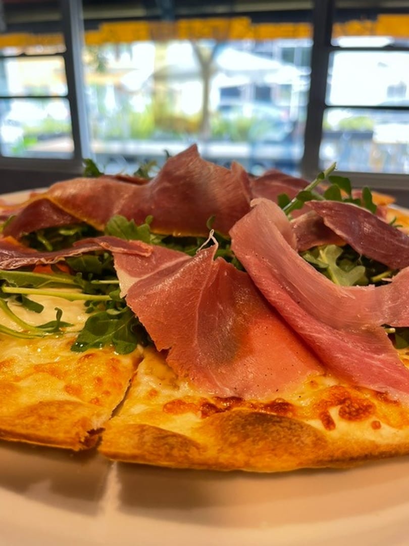 Delicious pizza with thinly sliced prosciutto and fresh arugula on a white plate.