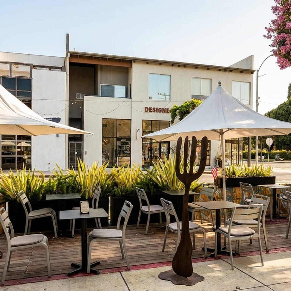 Outdoor patio dining area with tables, chairs, umbrellas, and planters, next to a building.