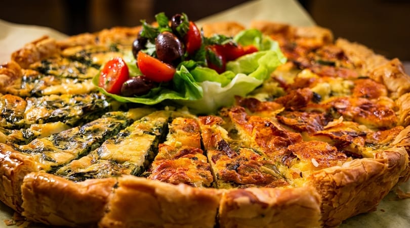 Savory quiche with spinach and cheese, garnished with a fresh salad of lettuce, tomatoes, and olives.