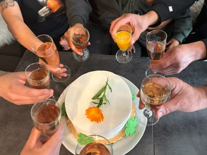 People toasting with champagne and orange juice around a white cake with an orange flower.
