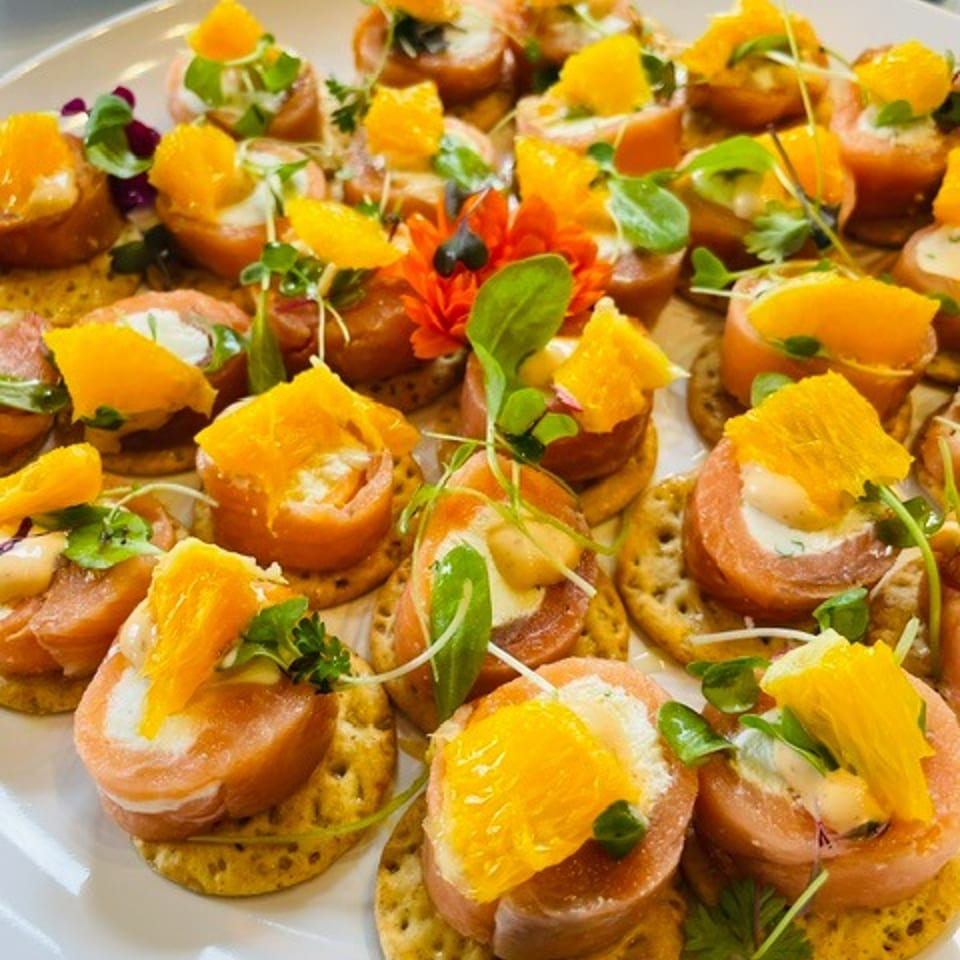 Plate of colorful crostini topped with creamy spread, orange segments, microgreens, and edible flowers.