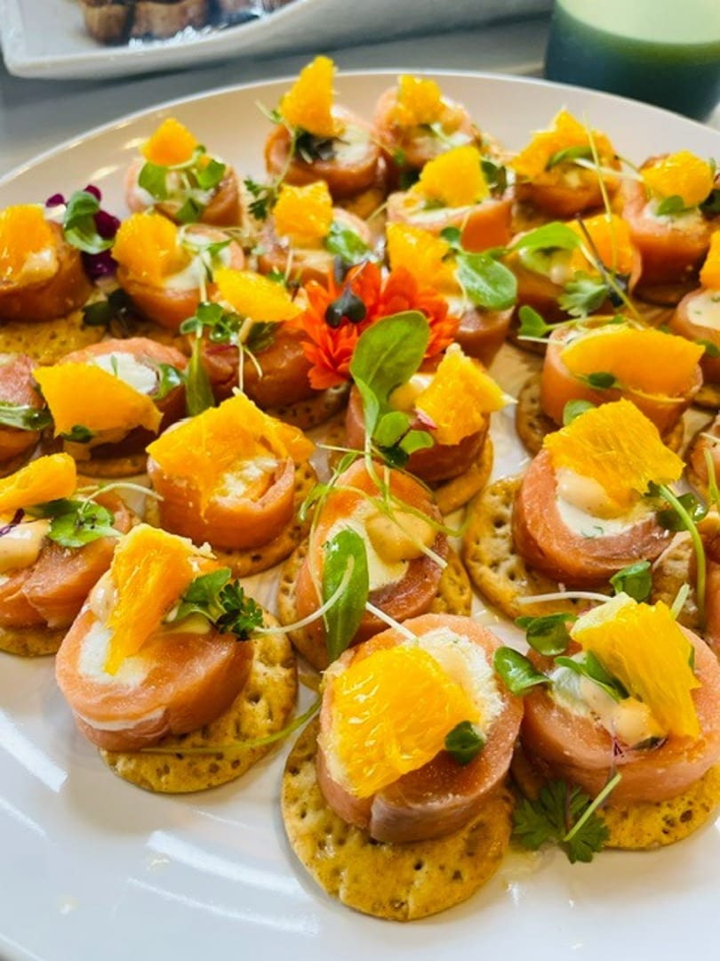 Plate of salmon and cream cheese appetizers on crackers, garnished with orange and microgreens.
